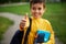 Focus on the schoolboy`s hand with thumb up. Out of focus adorable schoolboy showing a thumb up , smiling, standing with backpack