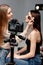 Focus of tripod with digital camera near happy makeup artist applying face powder on beautiful model