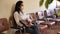 Focused adult hispanic woman in protective face mask sitting on chair in office corridor, waiting for job interview