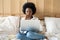 Focused Afro-American woman in white shirt relaxing after work, eating popcorn while watching horror or thriller movie on laptop,