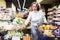Focused aged woman choosing green asparagus in supermarket