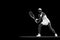 Focused athlete in tennis gear executing powerful forehand swing against black studio background. Monochrome filter.