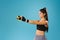 A focused athletic girl in a black top stretches a rubber band in front of her to train her arms against a blue