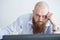 A focused bald man with a red beard stares intently at the camera. Male manager in a white shirt is angry at work.