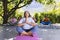 Focused biracial senior woman practising yoga with friends in sunny garden, copy space