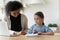 Focused biracial woman helping small child with study at home.