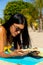 Focused biracial woman in sunglasses lying on sunny beach reading book