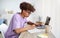 Focused black teenager in glasses studying online from home, writing in notebook, using laptop pc at table