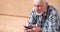 Focused elderly man holding mobile learning digital technology sitting on couch. Pensive grandfather chatting using smartphone