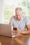 Focused elderly man using smartphone and laptop