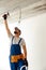 Focused electrician in uniform using hammer while attaching wire to ceiling, installing light fitting in apartment