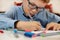 Focused face of a boy in a blue shirt and glasses while painting the picture. The boy is holding a felt-tip pen in his hand.