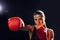 Focused female boxer in red boxing gloves training and looking away on black.