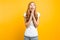 Focused girl asks God to help her, holding hands near her face, wishes good luck, on a yellow background