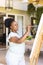 Focused happy senior african american woman holding palette painting on canvas at home, copy space