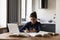 Focused Indian woman holding phone, writing notes, studying online