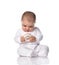 Focused infant baby toddler in white onepiece overall sits on the floor occupied with donut toy in hands
