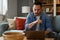 Focused male computer programmer holding eyeglasses and working over laptop seriously while sitting on sofa. Young pensive