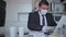 Focused male in disposable personal protective equipment working in business office using laptop, new normal due to