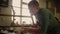 Focused man working with wooden plank indoors. Young man sawing wooden piece