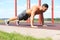 Focused muscular guy doing plank exercise outdoors