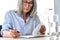 Focused older businesswoman in glasses reading partnership contract at table.