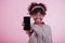 Focused photo. Holding black phone in hand. Attractive afro american woman in casual clothes at pink background in the