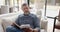 Focused senior biracial man sitting on couch reading book in living room at home, slow motion