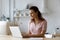 Focused serious freelancer woman using computer in kitchen