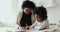 Focused small afro american girl doing homework with smiling mommy.