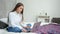 Focused smiling young freelancer woman working using laptop sitting on bed at cozy home