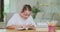 Focused teen girl at the desk, reads a book, tracking lines with finger Books, notebooks, pencil, laptop, lamp on the