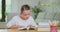 Focused teen girl at the desk, turnes the page, while reading a book Books, notebooks, pencil, laptop, lamp on the first