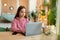 Focused teen girl studying online, using laptop, sitting at desk at home, having online lesson, typing on keyboard