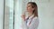 Focused woman doctor stands near spacious window in clinic