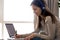 Focused woman in headphones writing notes, using laptop at home