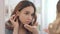 Focused woman putting on contact lenses in eye front bathroom mirror