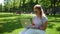 A focused woman in sunglasses is working with a laptop in a summer park.