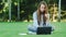 Focused woman using notebook for working online on green grass in summer park