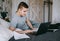 Focused young caucasian man holding paper documents on a bed with laptop