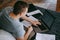 Focused young caucasian man holding paper documents on a bed with laptop