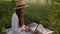 Focused young female freelancer in straw hat working typing on laptop computer sitting on field with green grass on