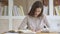 Focused young female teen student making notes in copybook.