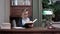 Focused young woman in glasses exploring the book sitting at the table in her study room