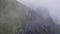 Fog and mist drifts over green vegetation on rugged coastal cliffs