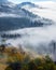 Foggy autumn morning. The lawn with the fruit trees and bushes. Landscape of high mountains and forests.