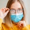 Foggy glasses wearing on young woman. Teenager girl in blue medical protective face mask and eyeglasses wipes blurred foggy misted