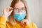 Foggy glasses wearing on young woman. Teenager girl in blue medical protective face mask and eyeglasses wipes blurred foggy misted