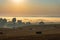 Foggy morning over an agricultural field with harvested wheat, bales of straw and a fog-filled valley with houses