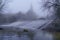 Foggy winter landscape, river with water falling down a waterfall, rocks and bare trees. Long exposure photo